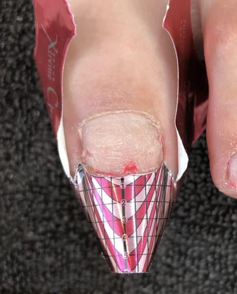 Step 2: Cut and customise a nail form to sit under the free edge of the nail. As the toenail is wider than a fingernail, use small curved scissors to cut and make the form wider. If the toe has a fleshy pad, stick the tab underneath or double up your form to hold down this skin.