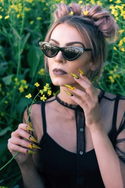 Deanna Stelmaschuk
"This entry represents me in many ways. Girly but dark, I love the contrast or pairing something dark or edgy with something soft and girly. I have a sunglasses obsession, a pair for every outfit. So naturally when going through all the photos I selected one with sunglasses. I've always wanted to do a canola field shoot to pay homage to where I grew up. I did the styling, hair , makeup, and nails for the shoot. For the nails I chose a sharp bright edgy design topped with flowers for softness on a short salon style stiletto. This is a design I would actually wear. I feel this set and shoot really captured my personality and my upbringing. My amazing niece Morgan Fraser took this beautiful photo. I'm very lucky to have such a talented up and coming photographer in my family bubble. Very handy in these challenging times."