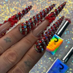 Luxurious nail design featuring long acrylic extensions decorated with red rhinestones and tiny bows, perfect for special occasions and nail art enthusiasts.