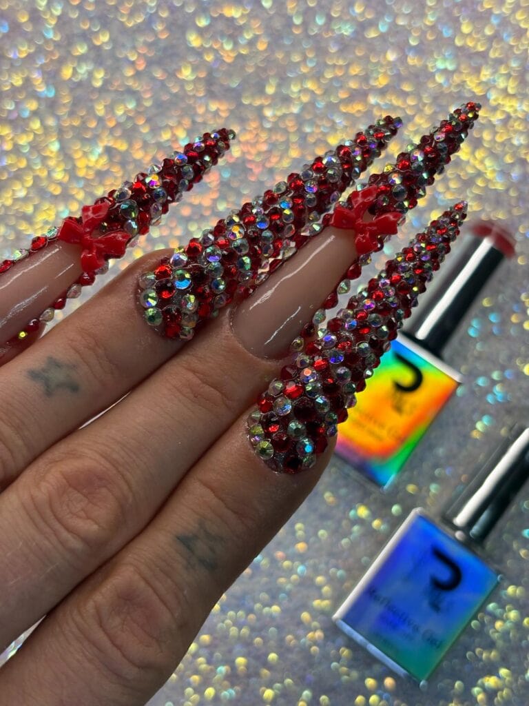 Luxurious nail design featuring long acrylic extensions decorated with red rhinestones and tiny bows, perfect for special occasions and nail art enthusiasts.